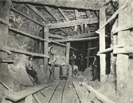 View inside a lead mine showing six miners with a car on a track.