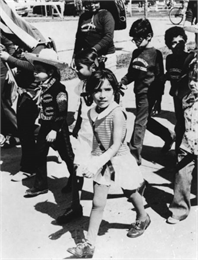 Children marching in a parade. One boy is wearing traditional Mexican clothing. Other children are wearing Bruce-Guadalupe Community School sweatshirts.