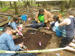 Four children and an adult next to an archaeological excavation unit