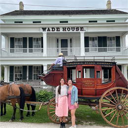 Two women standing in front of a red stagecoach
