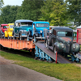 A freight train transporting yellow, red and blue vintage cars.