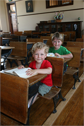 Two students sit in 1930s style school desks.