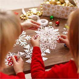 A mother and child crafting snowflakes out of white paper