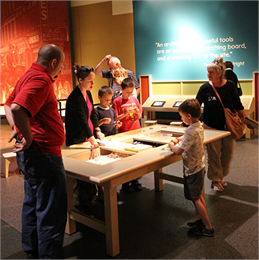 Numerous people looking at a light wooden table in a museum