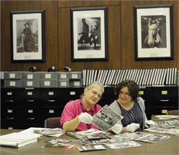 A researcher and staff member look at photos with white gloves in the Archives reading room.